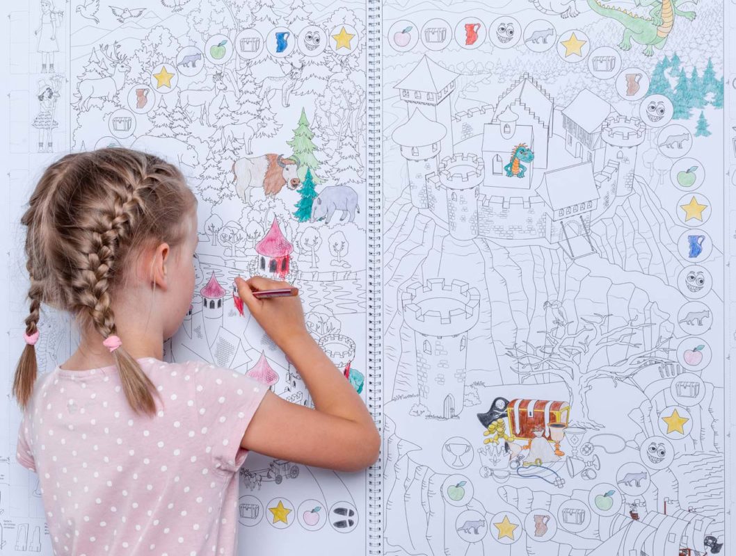Mädchen steht vor einer Wand, an der das Riesenspielmalbuch hängt, und malt ein Wimmelbild aus